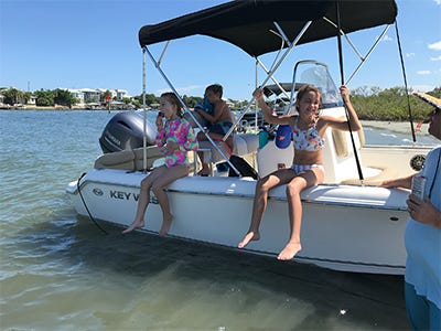 photo of a boat anchored on a sandbar with kids hanging off the side enjoying the water