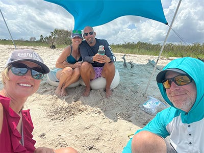 family hanging out at the beach under an umbrella and used a small shovel to dig higher ground to sit on